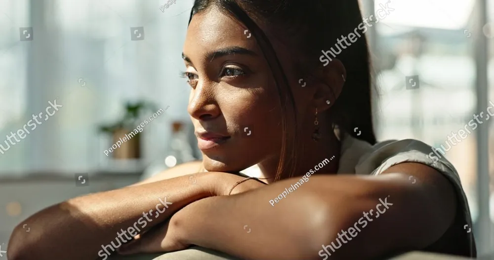 A woman resting her chin on her arms by a window, lost in thought