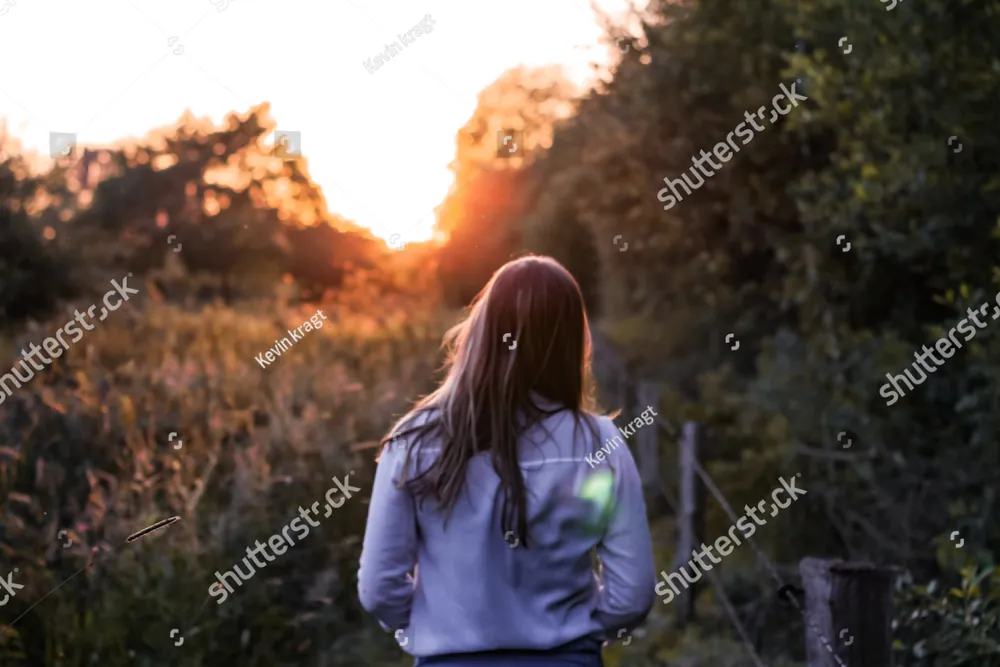 A woman walking through tall grass toward the setting sun