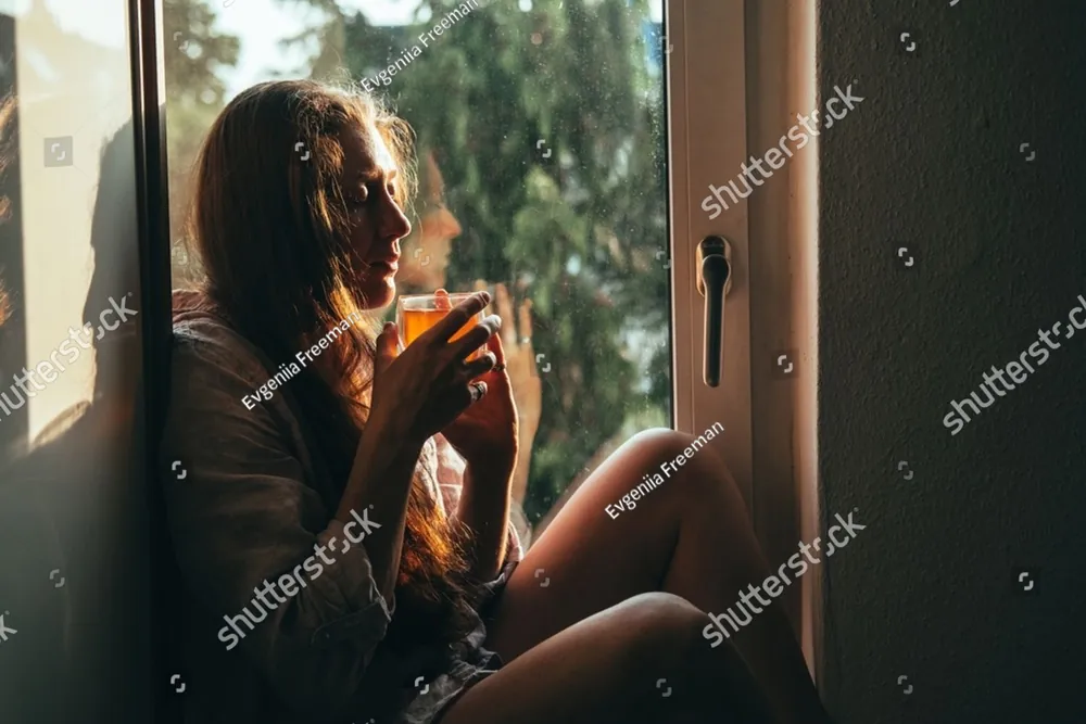 A woman sitting by a window holding a cup of tea