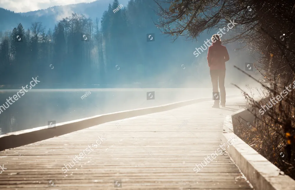 A person walking along a misty lakeside boardwalk