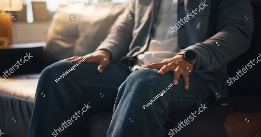 A man sitting on a sofa with his hands on his knees